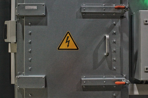 High voltage sign on the wall of a gate power plant. Industrial safety warning sign. Electricity switching station. Metal gray doors of  transformer box electrical substation