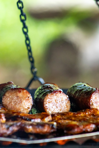 Gourmet sausage sizzling over the glowing embers of a fiery campfire barbecue.