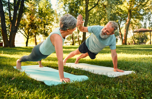 istock Teamwork during outdoors activity. Strong elderly couple in sportswear standing in plank position, giving high five, looking at each other and smiling. Concept of healthy retirement and active hobby. 1912058173