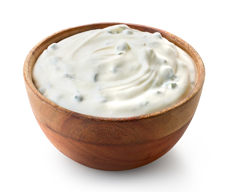 Wooden bowl of fresh sour cream dip sauce with herbs isolated on white background