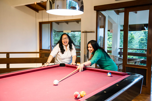 coach assisting her friend playing billiard indoor at home