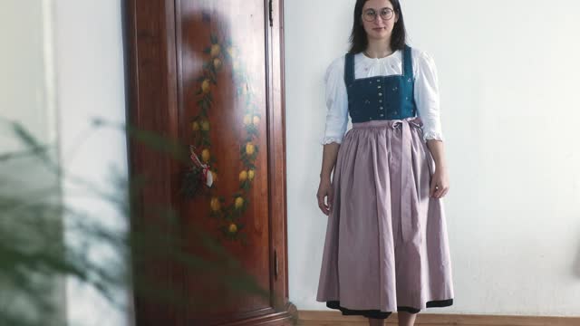 Model wearing a traditional antique Austrian dirndl dress with a pink apron in front of a hand-painted wardrobe, Salzburg, Austria
