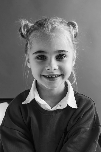 Portrait of a cute female child looking straight at camera and smiling. Monochrome photography concept.