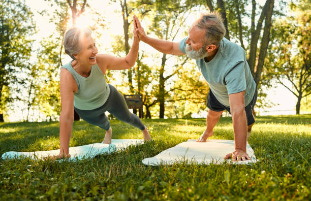 istock Fitness training on retirement. Healthy elderly man and woman making high five gesture while standing in plank position. Two pensioners smiling and participating during workout at green sunny park. 1912106675