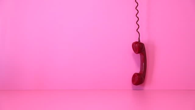 Old red telephone handset swinging at pink background