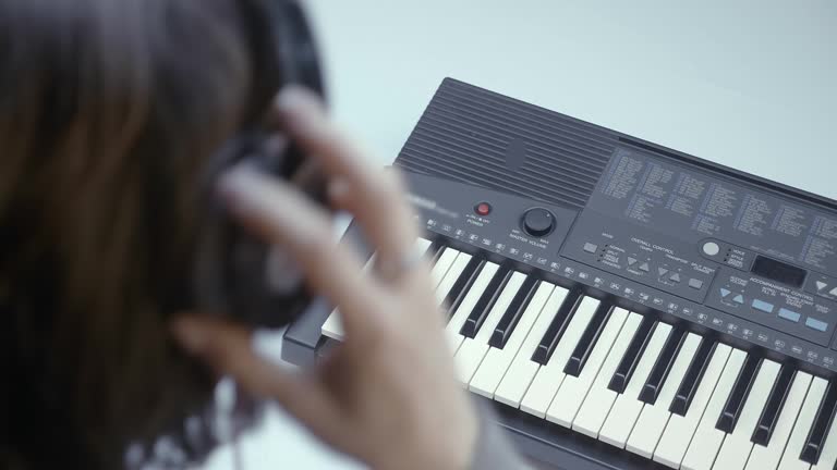 Woman playing on a synthesizer keyboard while listening to it on headphones