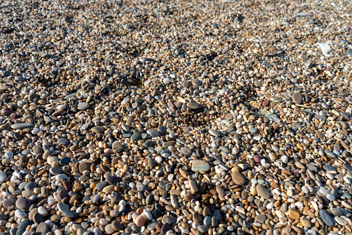 Background of colorful, rounded stones on a beach illuminated by the sun.