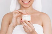 Young smiling woman in white towel after shower taking moisturizing cream with the hand holding jar