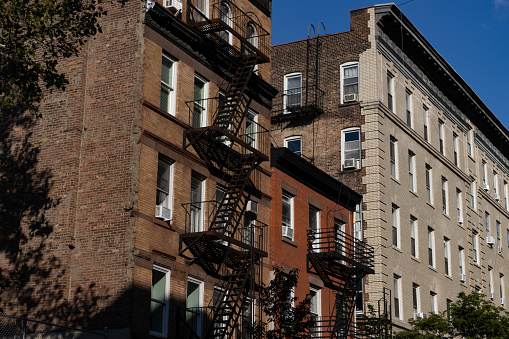 A row of old brick apartment buildings with fire escapes along a street on the Lower East Side of New York City