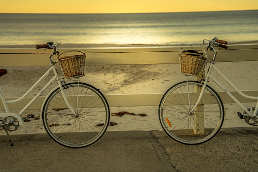 Two bicycles are silhouetted against the backdrop of a glowing orange-and-pink sunset at the beach