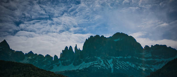 istock Scenic landscape featuring tall snow-capped mountains, partially obscured by wispy clouds. 1912256176