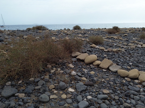 An idyllic coastal landscape featuring a vast collection of rocks and pebbles situated on the shoreline adjacent to a small boat