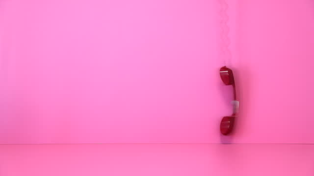 Old red telephone handset swinging at pink background