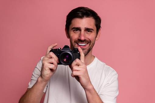 Portrait of a handsome young man holding a camera and smiling while standing against pink backgr