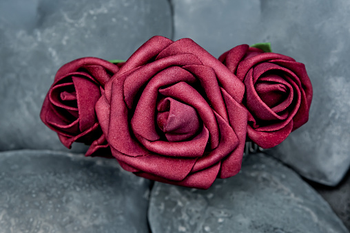 Satin faux fabric red roses on a stony background.