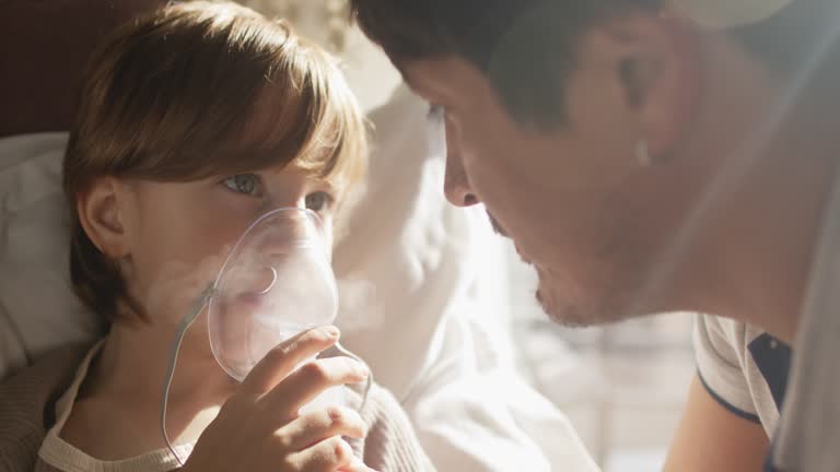 Sick child with father makes inhalation with nebulizer at home in bed with asthma, flu, cold, covid, bronchitis or pneumonia, virus or infection