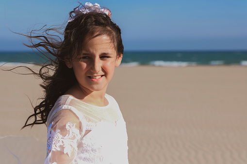 Girl smiling on the beach with her hair blowing in the wind, after her communion.