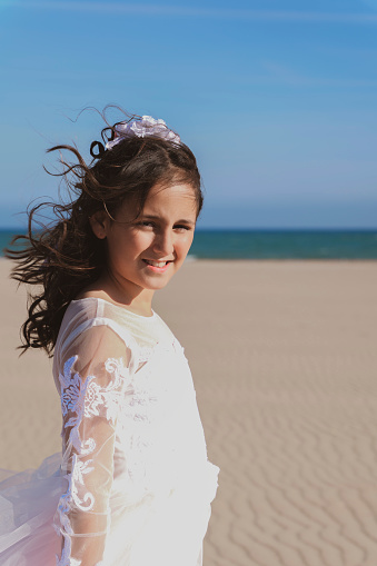 Girl smiling on the beach with her hair blowing in the wind, after her communion.