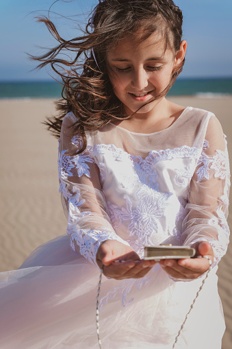 Girl clutching her catechism book and rosary on the beach at her communion.