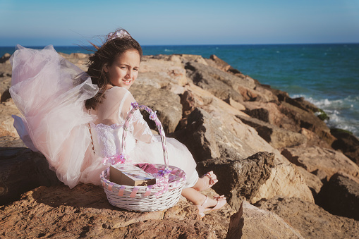 Girl sitting on rocks on the beach, with her communion dress and basket.
