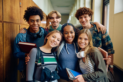 Multiracial group of happy classmates at high school hallway looking at camera.