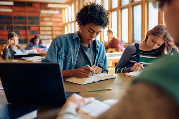 istock Black high school student learning with friends in a library, 1912514197