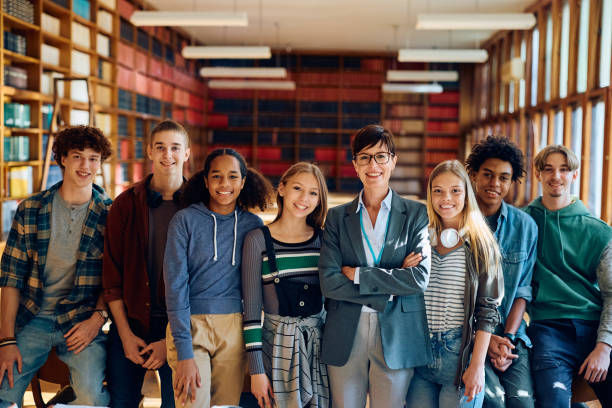 istock Confident high school teacher and her students in library looking at camera. 1912515750