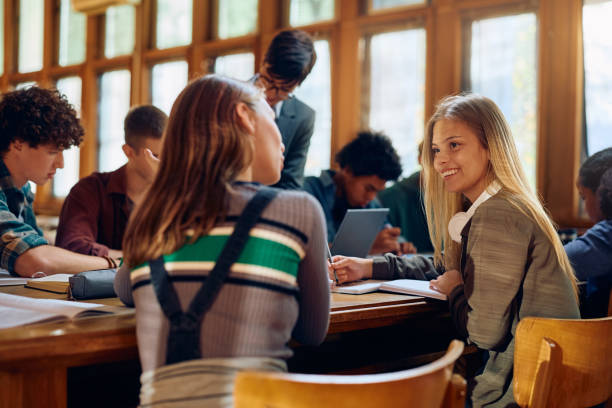 istock Happy high school student talking to her friend during a class in library. 1912516786
