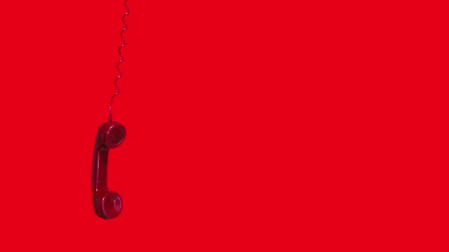 Old red telephone handset swinging at red background