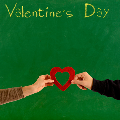 Young couple holding heart shape on green blackboard for Valentine's Day.