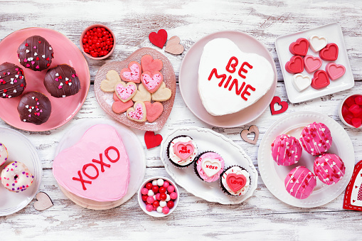 Valentines Day table scene with a selection of fun desserts and sweets. Above view on a white wood background. Love and hearts theme.