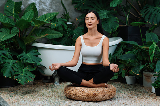 Young woman doing morning yoga and meditation in natural garden with plant leaf, enjoying the solitude and practicing meditative poses. Mindfulness activity and healthy mind lifestyle. Blithe