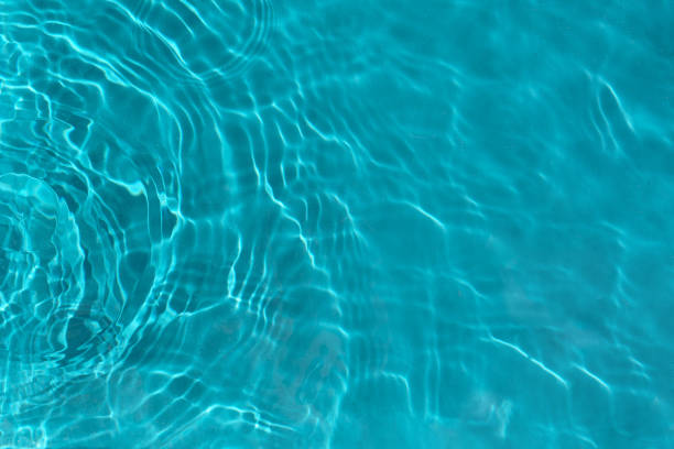 Waves on the light of the pool water. Swimming pool with blue water. Water surface texture. View from above.