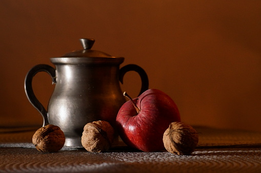 Background with fruits; an apple and three walnuts next to a silver metal bowl