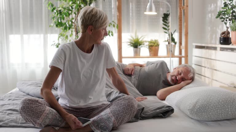 Dissatisfied mature woman using phone while her husband is sleeping