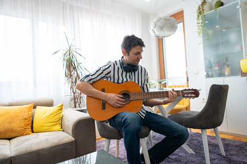 Shot of a man playing acoustic guitar at his apartment