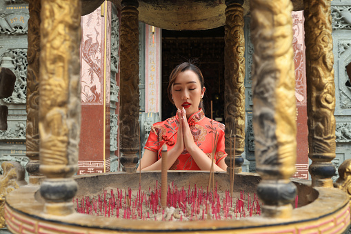 Young asian woman wearing red qipao cheongsam dress pray with god at the shrine, Chinese New Year