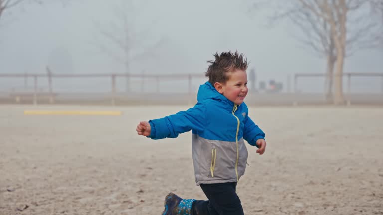 SLO MO Cheerful Boy with Spiky Hair in Winter Coat Running Playing with Cute Dogs in Playground in Foggy Weather