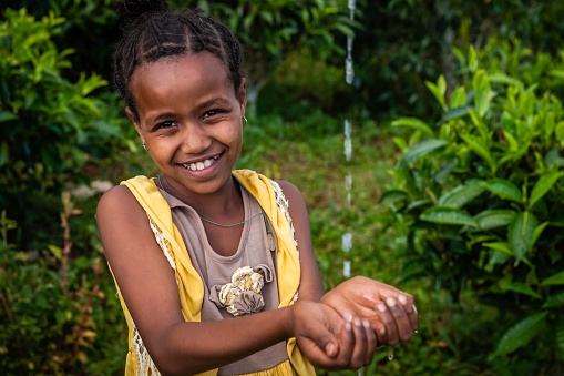 Happy African little girl drinking fresh water in village in Central Ethiopia. Potable water is very precious in Africa - women and children often walk long distances to bring back jugs of water that they carry on their back.