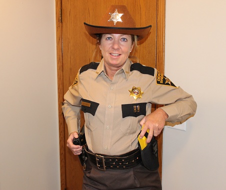 Sheriff's deputy, Mature, female, white, Blonde, in brown uniform indoors
