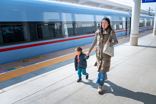 Delightful moment captured during a break on the platform, as a lively two and a half year old boy shares joy with his Chinese mother. The vibrant scene unfolds beside a striking blue train, adding a touch of adventure to this heartwarming snapshot