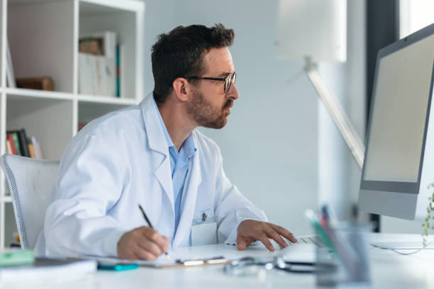 istock Mature male doctor working with computer while writing notes in the medical consultation 1913063324