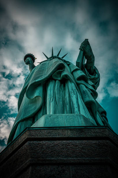 From a worm's-eye view, the Statue of Liberty looms majestically against the sky, its torch held high as a beacon of freedom. The perspective emphasizes the monument's towering presence, symbolizing liberty and welcoming all with a sense of grandeur from the ground up.