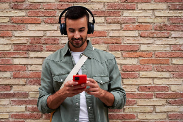 istock Caucasian man smiling while using phone to send online messages and listen music. 1913118077