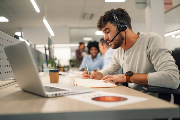istock Handsome man with headset working on a laptop and talking with clients 1913125760