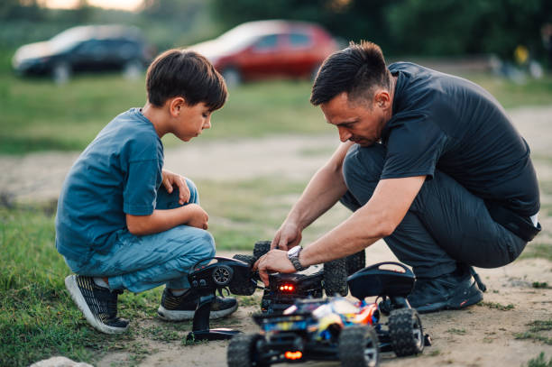 istock Boy watching his father fixing his overturned remote controlled toy car 1913125776
