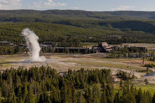 A high angled unique view of Old Faithful Geyer erupts next to Old Faithful Inn at Upper Geyser Basin in Yellowstone National Park in Wyoming USA