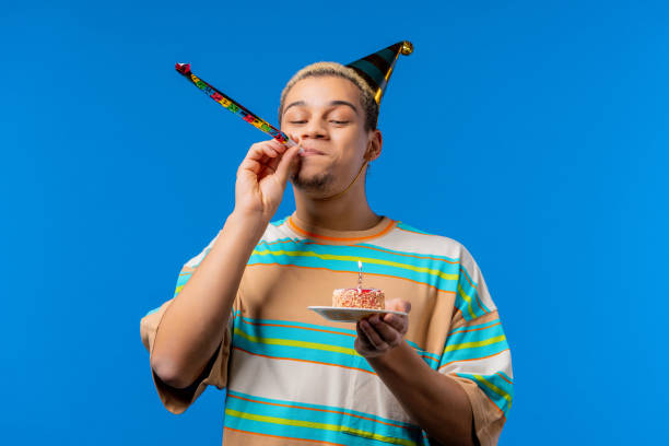 Happy birthday man making wish - blowing candle on cake. Curly haired guy