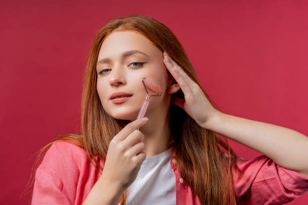 young woman with rose quartz stone roller on pink background. facial self care - quartz caucasian one person energy fotografías e imágenes de stock