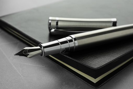 Stylish fountain pen, cap and leather notebook on light grey textured table, closeup